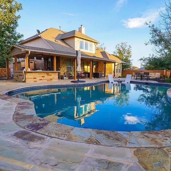 Outdoor kitchen, pergola, and pool framed by flagstone paving in Steiner Ranch