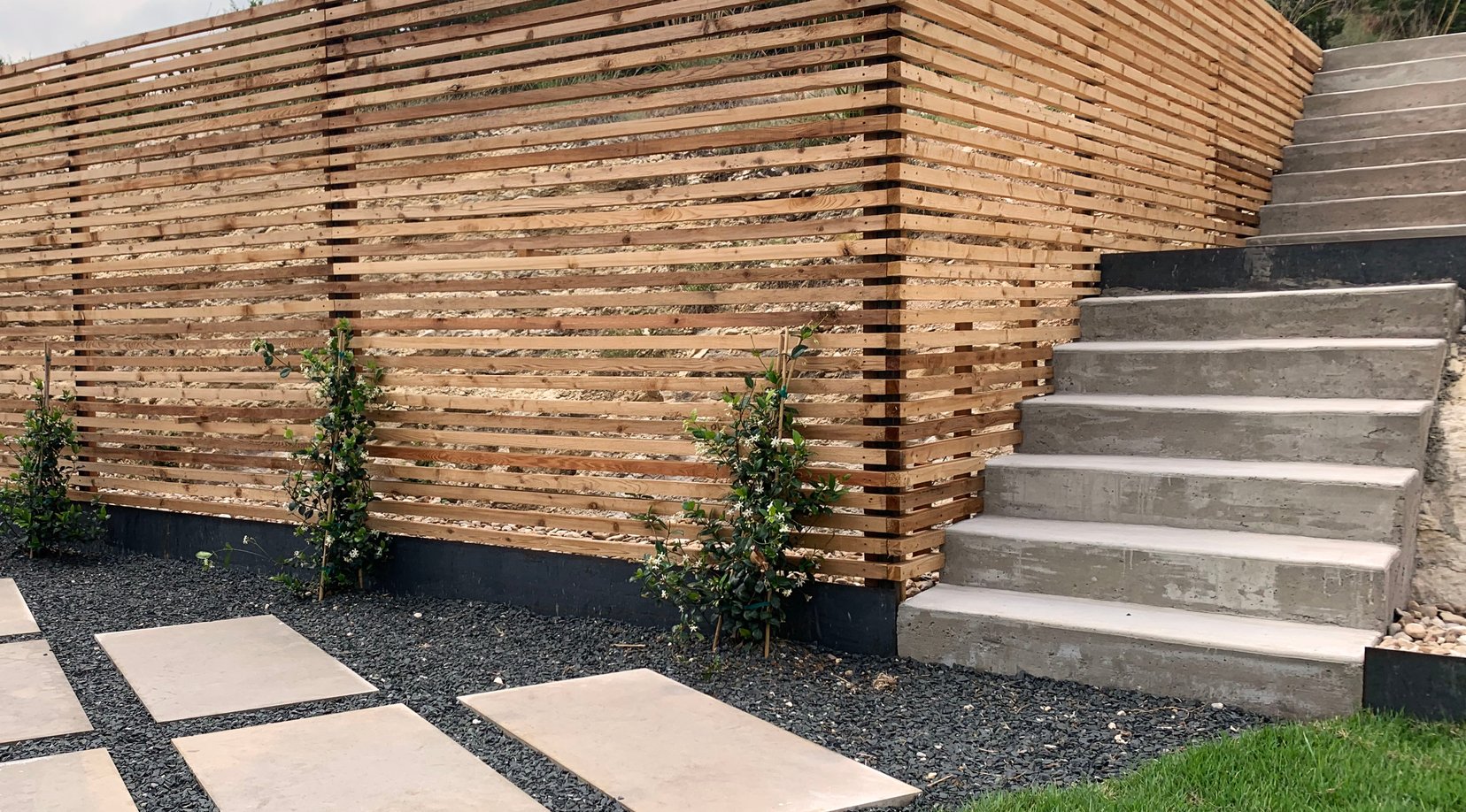 Poured concrete steps rising through the grade beside the cedar slat fence