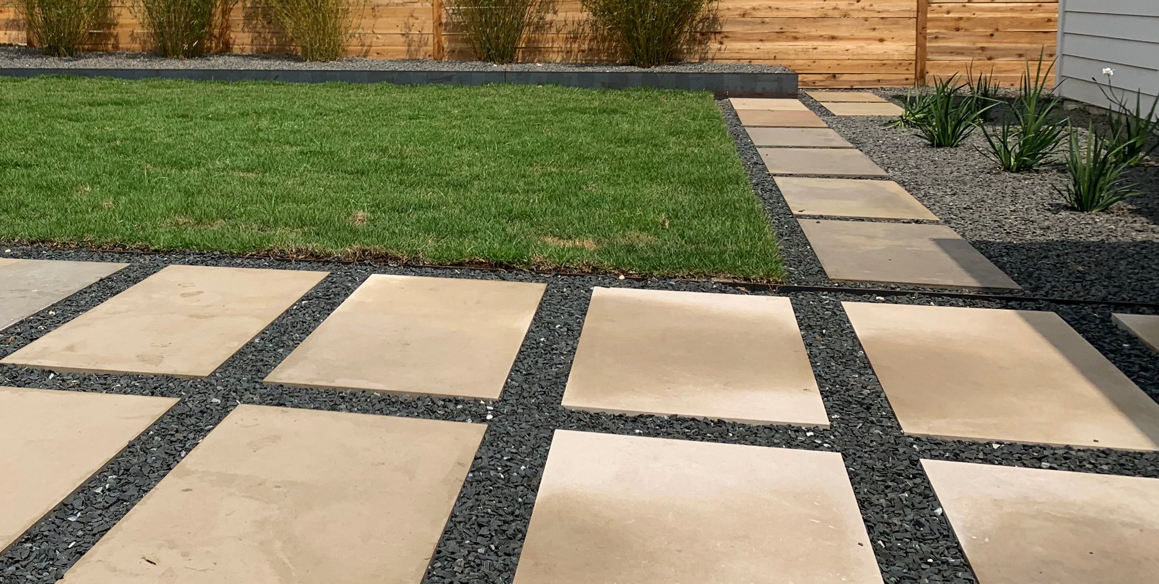 Sod, stepping stones, and gravel set against the horizontal cedar slat fence and planting beds