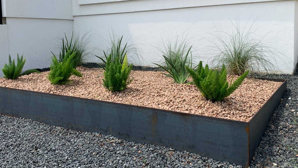 Freshly prepped steel-edged planter bed with gravel and ornamental plants in Westlake Hills