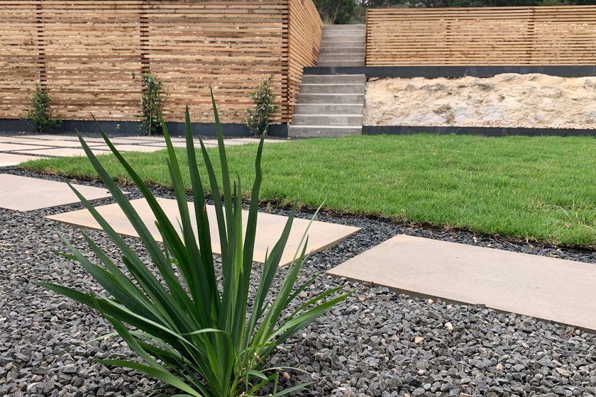 Terraced Westlake Hills backyard with stepping stones, gravel, sod, concrete steps, and a horizontal slat fence