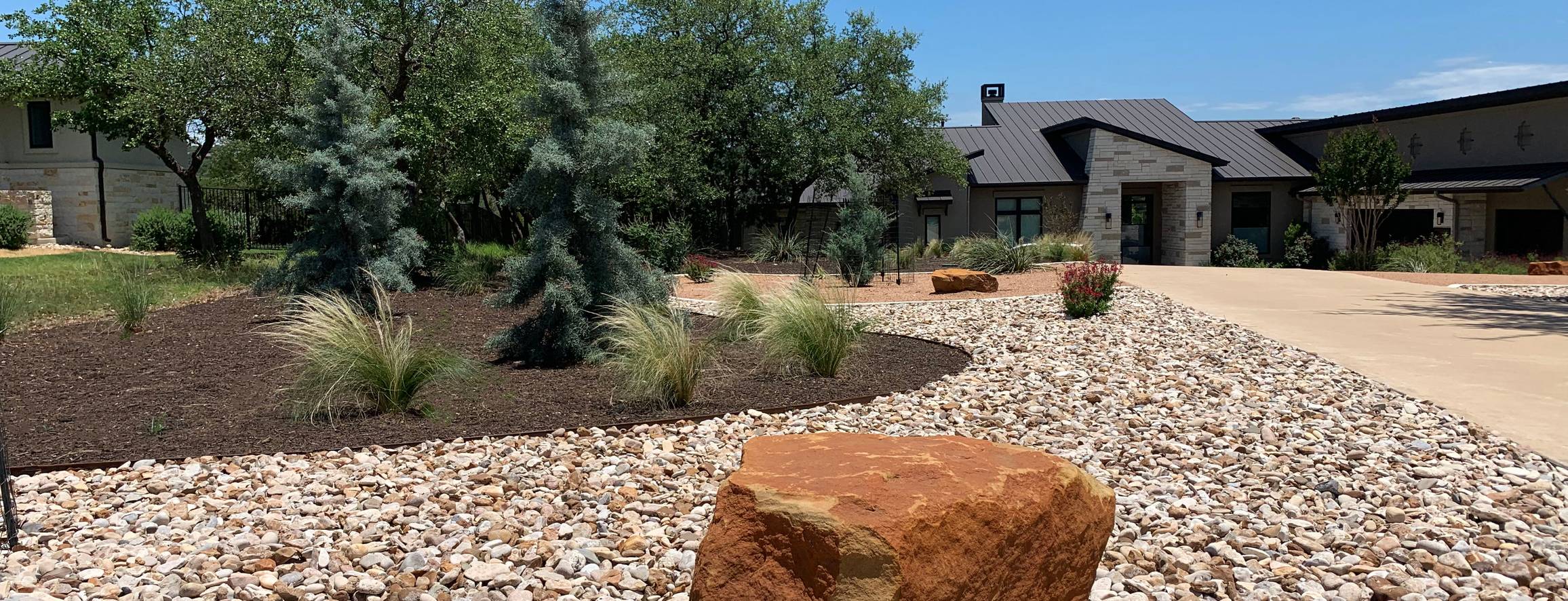 Dripping Springs hill country xeriscape with crushed granite, river rock, and mulch zones around a live oak by Thrive Landscape and Design