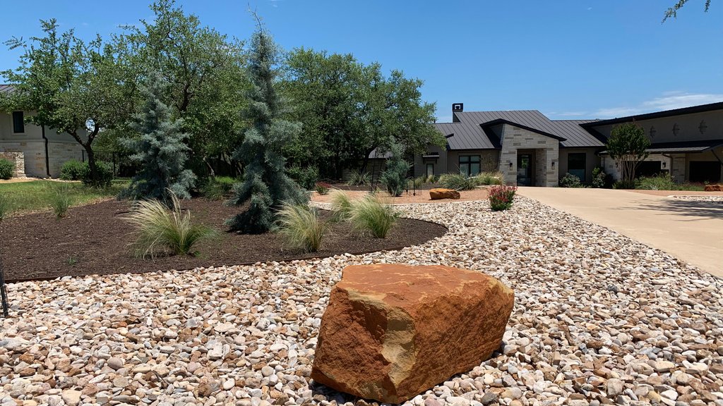 Hill Country home with a wide driveway approach, river rock, and native plantings in Dripping Springs