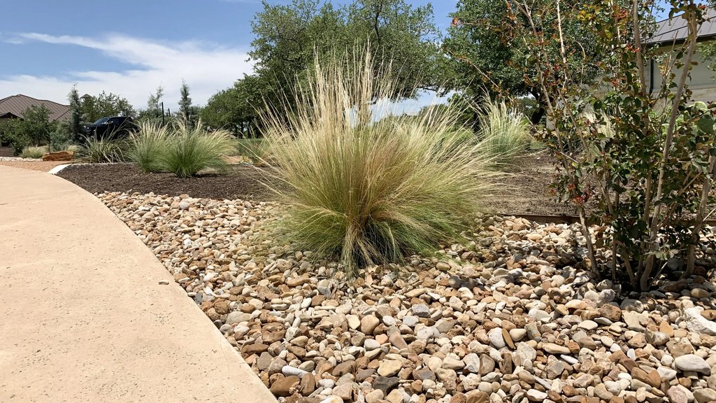 River rock and ornamental grasses laid out across a Dripping Springs Hill Country bed