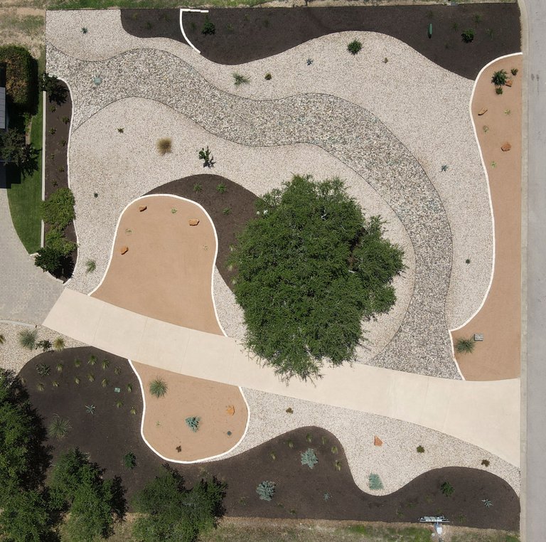 Aerial xeriscape design with crushed granite, river rock, and mulch zones around a live oak in Dripping Springs