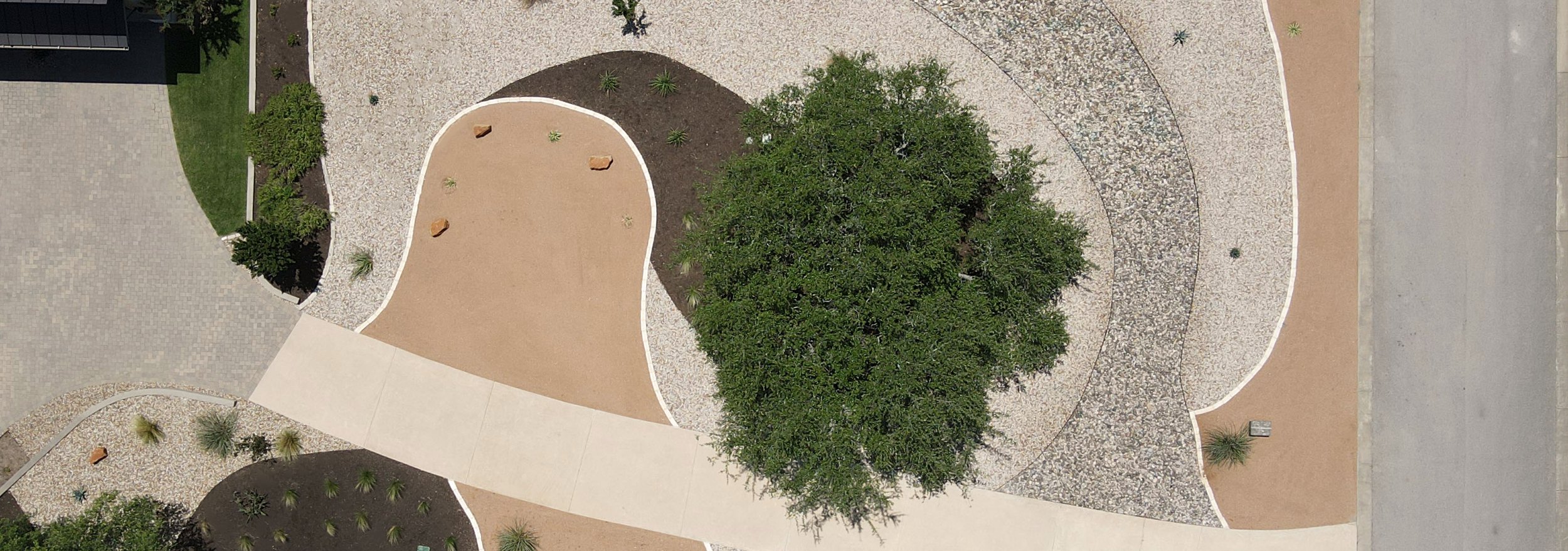 Aerial view of the completed lawn-free native xeriscape, its crushed granite, river rock, and mulch zones curving around the preserved live oak