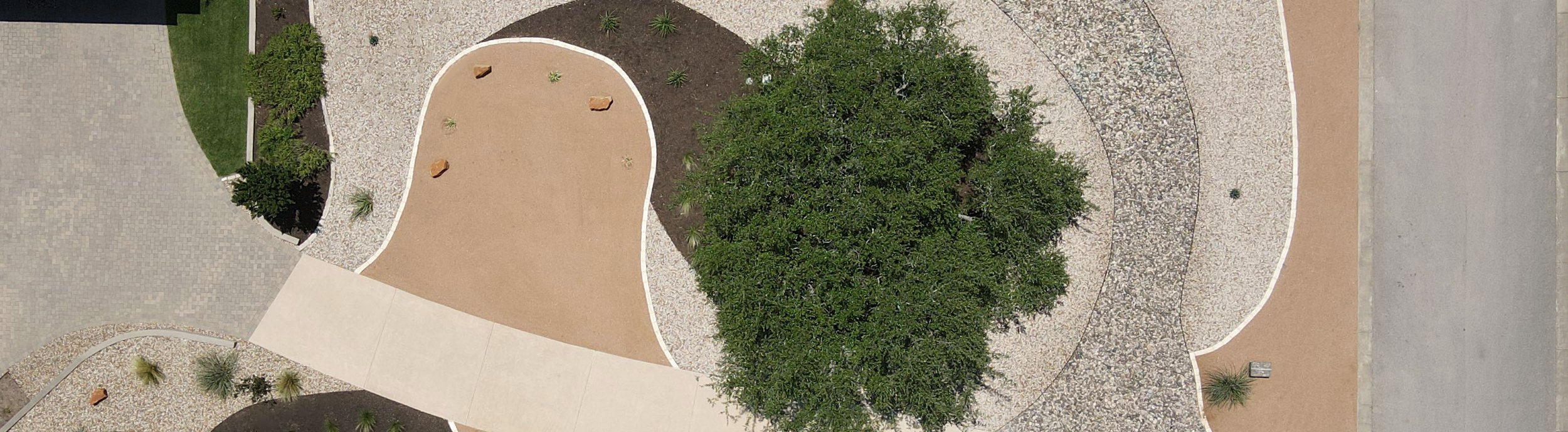 Aerial view of a lawn-free native xeriscape in Dripping Springs, TX with crushed granite, river rock, and mulch zones curving around a mature live oak